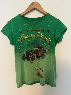 Grön t-shirt med biltryck och text - Cool grön t-shirt med färgskiftning och tryck av en retro bil, spelkort och texten '13th Annual Crown Picnic' i guld. T-shirten har korta ärmar och rund hals. Perfekt för dig som gillar unika motiv och streetstyle.