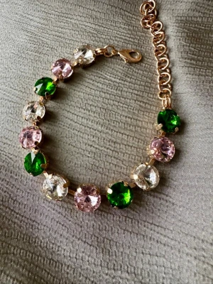 Armband med gröna, rosa och klara stenar - Glittrande armband med stora runda pärlor i grönt, ljusrosa och klart. Guldfärgad kedja och lås ger en lyxig känsla. Perfekt för dig som gillar färg och vill sticka ut med accessoarer. Stenarna är infattade i metall och armbandet har justerbar längd.