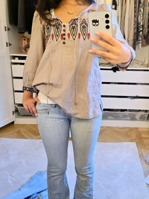 Trekvartsärmad Beige boho-blus med brodyr - Säljer en grå/beige boho-inspirerad blus med svart och röd brodyr upptill. Pärlorna på snöret har börjat lossna men utöver det är blusen i bra kondition! 💕 pris kan diskuteras