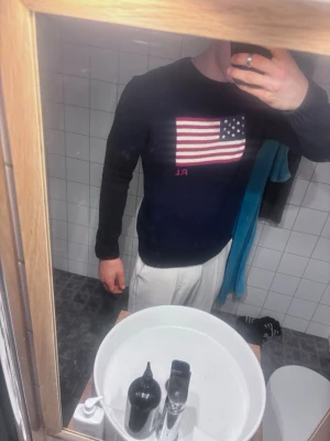 Mörkblå stickad tröja USA Polo Ralph Lauren - Säljer en mörkblå stickad tröja från Polo Ralph Lauren med amerikansk flagga på bröstet och RL-broderi. Tröjan har rund halsringning och ribbstickade muddar. Perfekt för dig som gillar klassisk och stilren design.