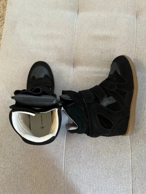 Isabel Marant - Svarta wedge sneakers från Isabel Marant med högt skaft och kardborreband. Skorna har en cool design i mocka och läderdetaljer samt en beige gummisula. Insidan är vit och skorna har en chunky siluett som sticker ut.