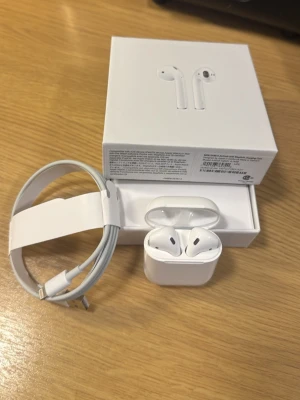 Vita trådlösa hörlurar - Säljer ett par vita vita headphones med laddningsetui och laddningskabel. Hörlurarna är trådlösa och har en stilren, minimalistisk design i blank plast. Perfekta för musik, poddar och samtal. Levereras i originalförpackning.