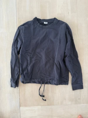 Mörkblå sweatshirt med dragsko - En enkel och stilren mörkblå sweatshirt från Weekday. Tröjan har rund halsringning, långa ärmar och en unik dragsko i nederkanten för justerbar passform. Tillverkad i mjuk bomull som känns skön mot huden. Perfekt för en avslappnad och trendig look.