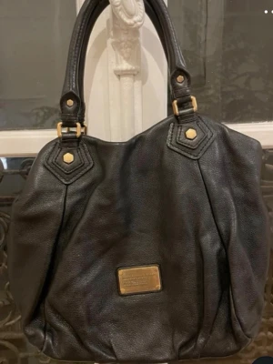 Svart handväska från Marc by Marc Jacobs - Snygg svart handväska i mjukt läder från Marc by Marc Jacobs. Väskan har guldfärgade metalldetaljer, dubbla handtag och ett stort huvudfack. Väskan är i perfekt storlek för sleep ovet eller liknande. Säljer dem då den aldrig kommit till användning 