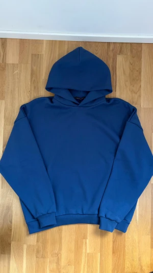 Blå hoodie från Unionkingdom - Säljer en stilren blå hoodie från Unionkingdom i storlek L. Den är använd 1-2 gånger. Hoodien har en klassisk passform med huva och ribbade muddar vid ärmslut och nederkant. Tillverkad i mjukt material som känns skönt mot huden. Perfekt för en avslappnad look.