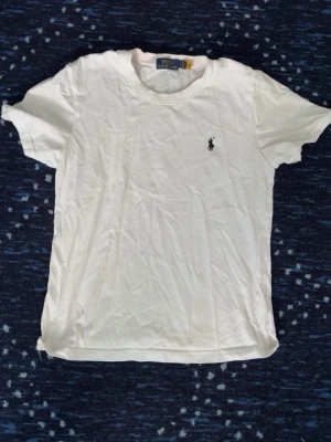 Vit t-shirt från Polo Ralph Lauren - Klassisk vit t-shirt från Polo Ralph Lauren med den ikoniska lilla loggan broderad på bröstet. T-shirten har rund halsringning och korta ärmar. Perfekt basplagg i mjuk bomull som funkar till allt.
