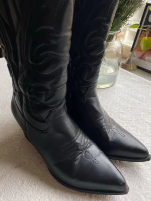 Svarta cowboy boots med broderi - Snygga svarta cowboy boots i läder med spetsig tå och klassiskt broderat mönster på skaftet och framtill. Högt skaft och dragkedja på insidan. Det är storlek 41 men jag som 39/40 tycker de passar ändå!