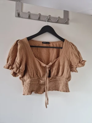 Beige croppad blus från Shein - Söt beige croppad blus från Shein med puffärmar och smockad midja. Toppen har v-ringning och knyt framtill, vilket ger en avslappnad men trendig look. Välanvänd men den är fortfarande i fint begagnat skick. Katt finns i hemmet
