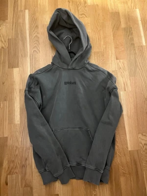 Mörkgrå hoodie från Gymshark - Snygg mörkgrå hoodie från Gymshark med stor huva och magficka. Tryckt Gymshark-logga i svart på bröstet och stort på ryggen. Oversized känsla och ribbade muddar vid ärmar och nederkant. Perfekt för chill eller gymmet.