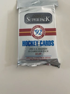 Score Super Pack NHL Hockeykort 1992 - Oöppnat paket med 35 NHL hockeykort från Score, Super Pack '92 U.S. Edition. Förpackningen är silverfärgad med röd och blå text och innehåller samlarkort från National Hockey League. Perfekt för dig som gillar sport och samlarprylar.