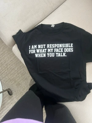 Svart t-shirt med vit text - Svart t-shirt med rund hals och vit tryckt text på bröstet: 'I am not responsible for what my face does when you talk.' Perfekt för dig som gillar humoristiska statement-plagg.