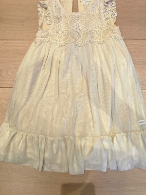 Vit spetsklänning från Newbie - Supersöt vit klänning från Newbie i storlek 128. Klänningen har ett detaljerat spetsliv med blommönster och volangärmar samt ett skirt, lätt tyg i kjolen. Perfekt för speciella tillfällen eller när du vill känna dig extra fin.