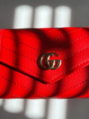 Röd quiltad plånbok från GG - Säljer en snygg röd plånbok från GG i quiltat läder med GG-logga i guld framtill. Plånboken har ett kuvertformat lock och stilrena sömmar i zigzag-mönster. Perfekt accessoar för dig som gillar lyxiga detaljer och trendig design.