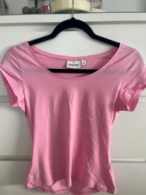 Rosa t-shirt från Kappahl - En enkel och mjuk rosa t-shirt från Kappahl med rund halsringning och korta ärmar. Perfekt att matcha med jeans eller kjol för en avslappnad look. Tillverkad i bomull för en skön känsla.