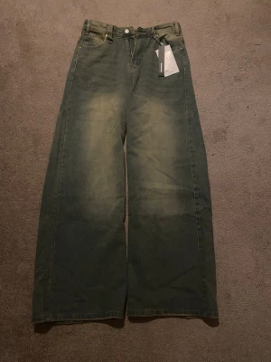 Ljusblåa baggy wide leg jeans – Medium - Nyskick med tags kvar. Trendig baggy/wide leg passform i grön tvättad denim. Perfekta för loose fit/streetwear-look.  * Storlek: Medium * Färg: Grön tvättad denim * Skick: Oanvänd med tags * Passform: Baggy / wide leg