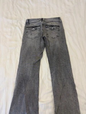 Grå bootcut jeans med fickdetaljer - Snygga grå bootcut jeans med klassiska fem fickor och coola detaljer på bakfickorna. Jeansen har en lätt tvättad look och raka ben som blir lite vidare nertill. Perfekta för en avslappnad och trendig stil.