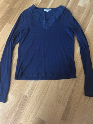 Mörkblå långärmad topp med spets - Mörkblå långärmad topp med v-ringning och dekorativ spets runt halsen. Tunn och mjuk kvalitet, perfekt för lager-på-lager. Enkel och stilren design som passar till mycket.