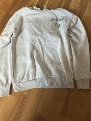 Grå sweatshirt med tryck Ma Chérie - Ljusgrå sweatshirt med svart tryck 'MA CHÉRIE' och en krona både fram och bak. Tröjan har rund hals, ribbade muddar och är tillverkad i mjukt bomullsmaterial. Perfekt för en avslappnad och trendig stil.