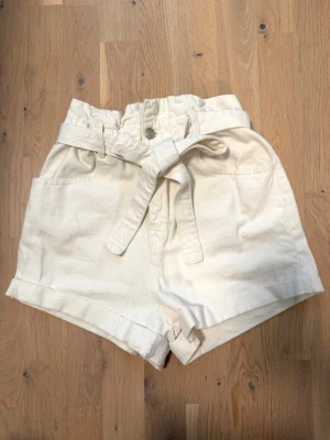 Vita högmidjade shorts med knytband - Snygga vita shorts med hög midja och knytband i midjan. Shortsen har breda ben, uppvikta benslut och stora fickor både fram och bak. Perfekta för varma dagar och ger en trendig look 🤍