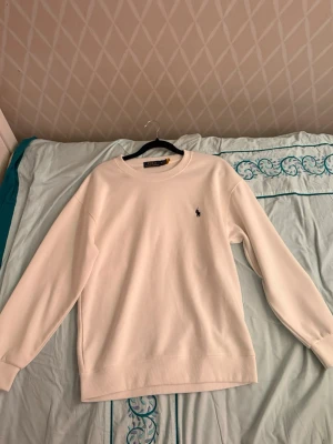 Vit sweatshirt från Polo Ralph Lauren - Klassisk vit sweatshirt från Polo Ralph Lauren med rund halsringning och broderad logga på bröstet. Tröjan har en avslappnad passform, långa ärmar och ribbade muddar vid ärmslut och nederkant. Perfekt för en clean och stilren look.
