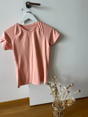 Ljusrosa t-shirt från Pro Touch - Säljer en ljusrosa t-shirt från Pro Touch med rund hals och korta ärmar. Tillverkad i ett mjukt och lätt polyestermaterial med DryPlus-teknologi som håller dig fräsch under träning eller vardag.