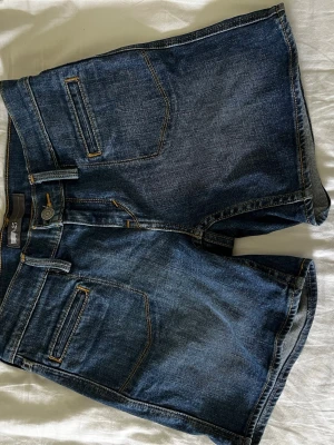Blå denimshorts från Levi's - Säljer ett par klassiska blå denimshorts från Levi's med snygga kontrastsömmar och flera fickor både fram och bak. Shortsen har en normal passform och är tillverkade i slitstark bomull. Perfekta för sommarens alla äventyr!