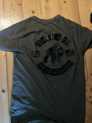 Olivgrön Gorilla Wear t-shirt - Säljer en olivgrön t-shirt från Gorilla Wear med stor gorilla-logga och text på ryggen samt liten logga fram. T-shirten har rund hals och korta ärmar, tillverkad i mjuk bomull som passar perfekt till en aktiv livsstil.