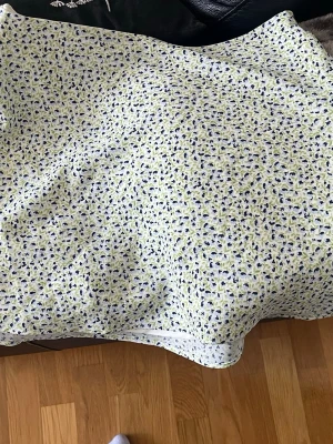 Blommig kortkjol i bomull - Söt kortkjol med småblommigt mönster i blått och grönt på vit botten. Kjolen är gjord i mjuk bomull och har en avslappnad passform, perfekt för varma dagar. helt ny aldrig använd. 