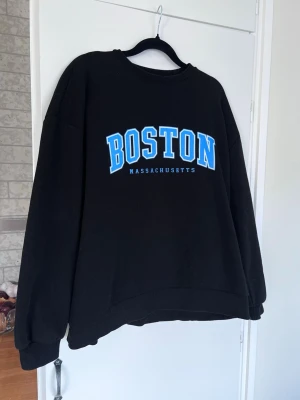 Y2K Oversized svart/blå streetstyle sweatshirt  - Svart streetstyle-vibe sweatshirt med blå text 'BOSTON MASSACHUSETTS'. Oversized fit och avslappnad streetwear-look. Sparsamt använd.