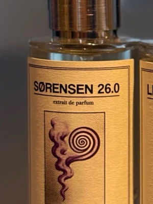 Sørensen 26.0 Extrait de Parfum - Unik parfym från Sørensen med namnet 26.0. Flaskan är genomskinlig med en stilren beige etikett och svart text. Locket är i metall och etiketten har en konstnärlig spiraldesign. Perfekt för dig som gillar exklusiva dofter.