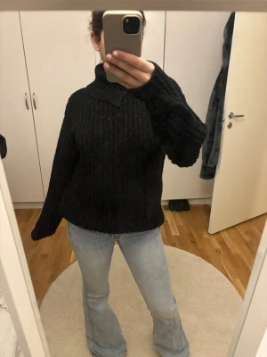 Svart stickad tröja med krage - Mysig svart stickad tröja med bred krage och långa ärmar. Tröjan har en avslappnad passform och är ribbstickad vilket ger en snygg struktur. Perfekt att matcha med jeans för en chill look.