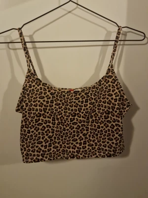 Leopardmönstrad croppad linnetopp - Snygg croppad linnetopp med leopardmönster och tunna axelband. Perfekt för dig som vill sticka ut och addera lite edge till din outfit. Toppen har en beige bas med bruna och svarta detaljer i mönstret.