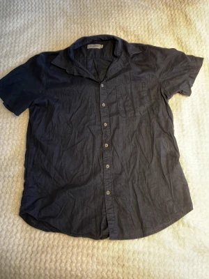 Mörkblå kortärmad skjorta Dressmann - Säljer en mörkblå skjorta med korta ärmar och klassisk krage. Skjortan har knappar framtill och en bröstficka. Perfekt till sommaren och enkel att matcha med olika outfits.