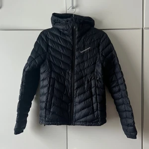 Mörkblå jacka från Peak Performance  - Snygg jacka från Peak Performance med huva och dragkedja framtill. Jackan har quiltad design och är lättviktig, perfekt för kyliga dagar. Logotyp på bröstet och smal passform som ger en modern look. Mörkblå nästintill svart! Knappt använd 