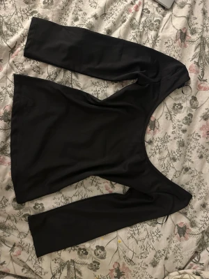 Svart långärmad topp med bred ringning - En svart långärmad topp med bred, djup ringning. Snygg och enkel design som passar till jeans eller kjol. Toppens material är mjukt och stretchigt, troligen bomull eller polyester. Perfekt för dig som gillar stilrena plagg med lite edge.