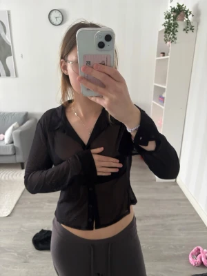 Svart transparent skjorta med knappar - Säljer en svart transparent skjorta med knappar framtill och klassisk krage. Skjortan är croppad och har långärmad passform. Perfekt för dig som gillar att sticka ut och vill ha något trendigt i garderoben.