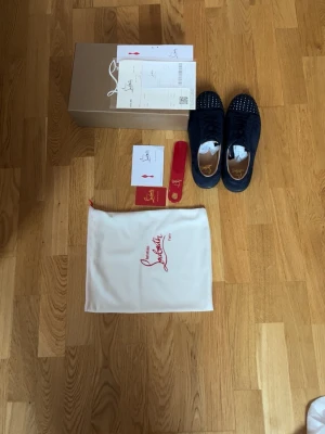 Marinblå Christian Louboutin sneakers - Snygga marinblå sneakers från Christian Louboutin med coola nitar på tån och klassisk röd detalj på sulan. Skorna har en låg profil och är tillverkade i mocka med läderdetaljer. Kommer med originalkartong, dustbag och tillbehör.