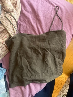 Olivgrön linnetopp från Gina Tricot - Säljer en enkel och stilren olivgrön linnetopp från Gina Tricot. Toppen har tunna axelband och ärmlös design, perfekt för varma dagar. Tillverkad i mjuk bomull som känns skön mot huden. Passar till både jeans och kjol för en avslappnad look.