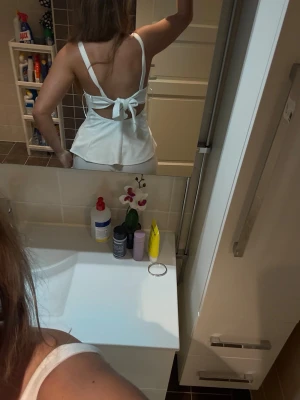 Vit peplum linnetopp med rosett - Säljer en vit peplum linnetopp med breda axelband och öppen rygg. Toppen har en snygg rosett och knytning baktill samt en figurnära passform upptill som blir utsvängd nertill. Perfekt för dig som vill ha en stilren och trendig look. Aldrig använd! Nypris 400kr