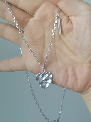 Silverfärgat hjärthalsband från Mindclassics - Unikt halsband i silverfärgad metall med ett hjärtformat hänge där det står 'may have a heart' och en liten smiley ingraverad. Kedjan är grov och har en Mindclassics-tag. Perfekt för dig som gillar statement-smycken och coola detaljer.