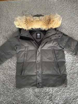 Canada Goose - (Pris kan diskuteras )Säljer denna canada goose vinterjackan pga av att jag har vuxit ur den. Den är i ett mycket bra skick, den har en skada vilket är att dom 3 knapp hålen har böjts(se bild) vilket går och fixa annars har den inga andra skador. 