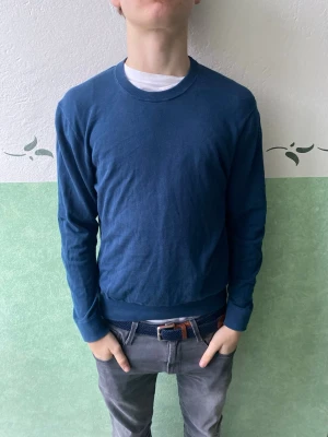 Mörkblå basic tröja från Riley - En enkel och stilren mörkblå tröja med rund halsringning och långa ärmar. Tröjan har ribbade muddar vid ärmslut och nederkant. Perfekt att matcha med jeans eller chinos för en clean look.