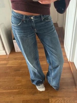 Zara lowwist jeans - Säljer ett par blåa jeans med hög midja och raka, vida ben. Klassisk femficksmodell med knapp och dragkedja framtill. Jeansen har en avslappnad passform och är gjorda i denim. Perfekta för en chill och trendig look.