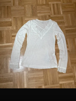 Vit långärmad topp med spets - Söt vit långärmad topp från Twist & Tango med v-ringning och spetsdetaljer runt halsringningen och ärmsluten. Tunn och mjuk i materialet, perfekt för lager på lager eller som den är. Enkel men ändå romantisk vibe.