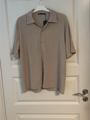 Beige kortärmad skjorta  - Säljer en stilren beige skjorta från Lager 157med korta ärmar och klassisk krage. Skjortan har knappar framtill och är gjord i ett mjukt material som känns skönt mot huden. Perfekt för dig som gillar en enkel och clean look. Ny pris 200