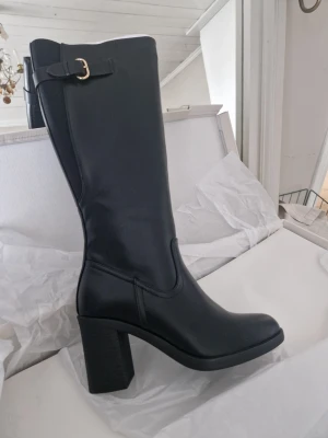 Svarta stövlar st 38  - Stilrena svarta stövlar med  dekorativt spänne upptill. 