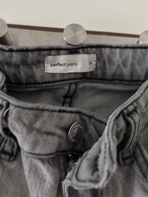 Grå jeans från Perfect Jeans (Gina tricot)  - Säljer ett par gråa jeans från Perfect Jeans (Gina tricot) i storlek 34. Jeansen har klassisk femficksmodell, raka ben och tydliga sömmar. Materialet är denim i bomull och färgen är en snygg tvättad grå nyans. Perfekta till uppklädning och avslappnad stil.