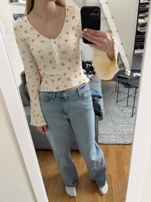 Söt blommig topp - Säljer en vit, söt, ribbad topp med rosa blommor på och knytning framtill. Den är vid längst ner på ärmarna. 