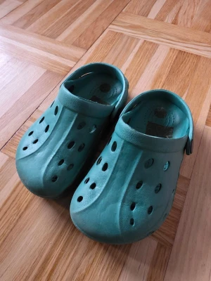 Turkosa tofflor i gummi - Säljer ett par turkosa tofflor i gummi med klassisk clog-design och ventilationshål över hela ovandelen. Perfekta för stranden.