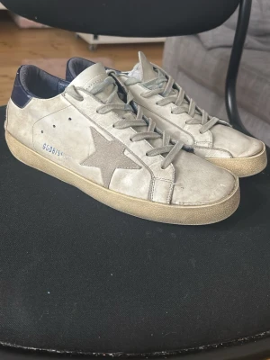 Golden Goose vita sneakers med stjärna storlek 41 - Snygga vita sneakers från Golden Goose med den ikoniska stjärnan på sidan och mörkblå detalj vid hälen. Priset kan diskuteras vid direkt köp. Funkar defenetift att andvända. Storlek 41, försöker skicka samma dag eller den efter, säljer för dem är för små för mig 👍